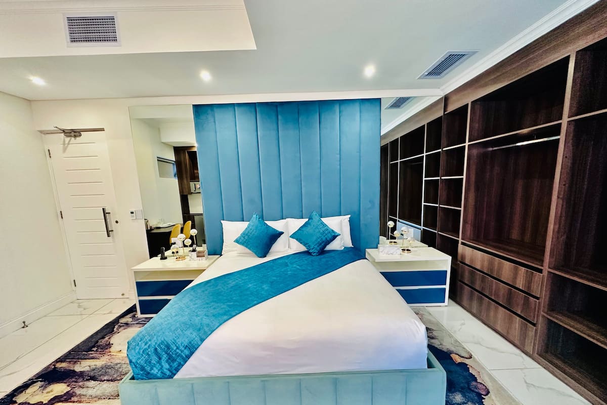 A modern bedroom with a large bed, a bedside table, a mirror, and a wardrobe.