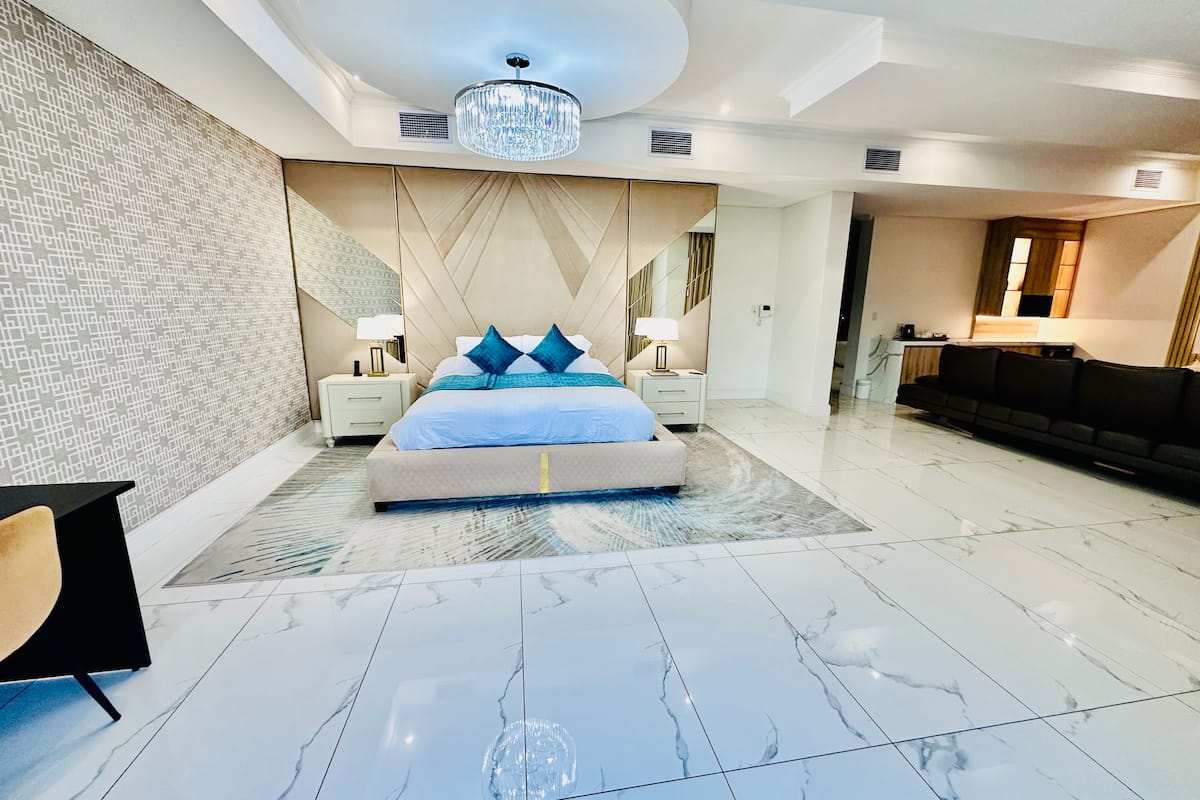 A modern bedroom with a large bed, a chandelier, and a bathroom visible in the background.