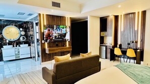 Quarto de hotel moderno com uma cama grande, um sofá, uma TV, uma área de cozinha e um banheiro com toucador e espelho.
