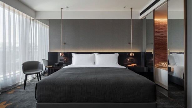 A modern hotel room with a large bed, a desk with a chair, a large window with curtains, and a brick accent wall. - Wanda Yi Hotel Xi'an The Linow (Xi'an)