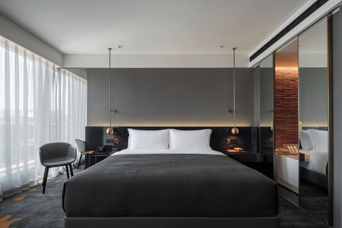 Camera d'albergo moderna con un letto grande, una scrivania con una sedia, un'ampia finestra con tende e un muro decorato con mattoni.