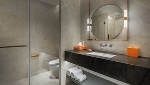 A modern bathroom with a glass shower enclosure, a black marble countertop, a round mirror, and a toilet. - Wanda Yi Hotel Xi'an The Linow (Xi'an)