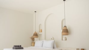 A minimalist bedroom with a large bed, two pendant lights, a vase, and a textured wall. - Villa Kasih Satu (Gili Trawangan)