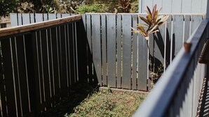 Ein Holzzaun mit vertikalen Lamellen und ein kleiner Gartenbereich mit Pflanzen.