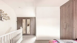 Een gang die leidt naar een slaapkamer met een houten garderobe en een witte leuning.