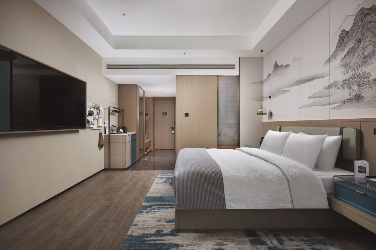 Camera d'albergo moderna con un letto grande, una TV a schermo piatto, una scrivania e un bagno visibile attraverso una porta aperta.