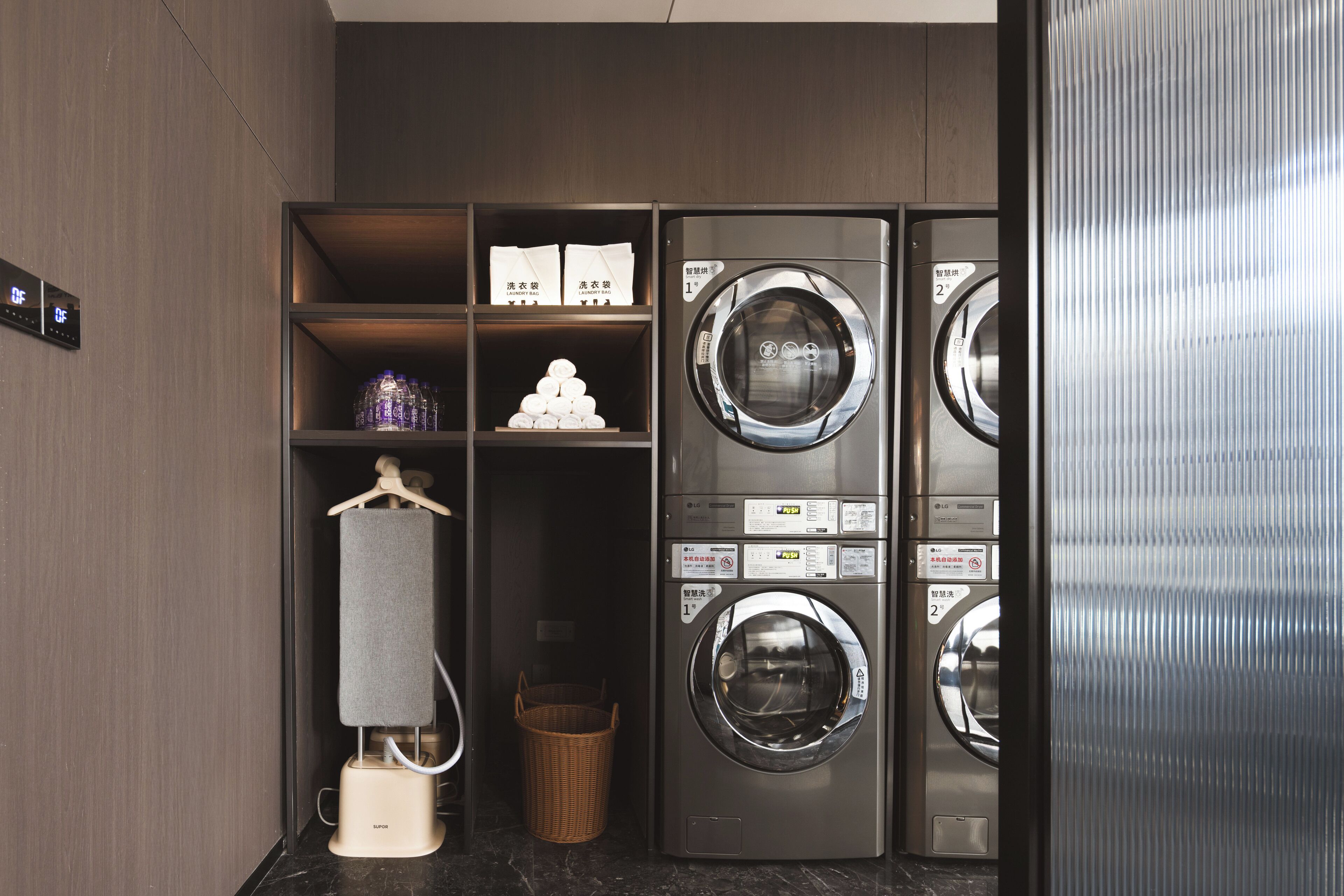 Une buanderie moderne équipée de deux machines à laver, d’un étendoir et d’étagères où sont pliés des vêtements, ainsi qu’un panier.