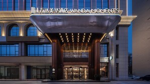 Une entrée d’hôtel moderne, avec une enseigne bien visible portant l’inscription « Wanda Moments ».