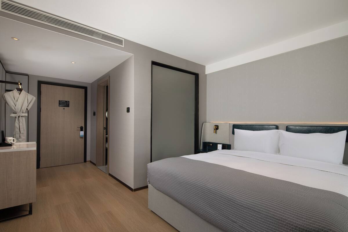 A modern hotel room with a large bed, a robe hanging on a rack, and a wooden floor.