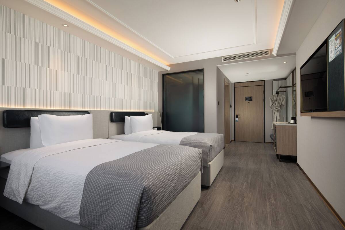 A modern hotel room with two beds, a large mirror, and a wooden floor.