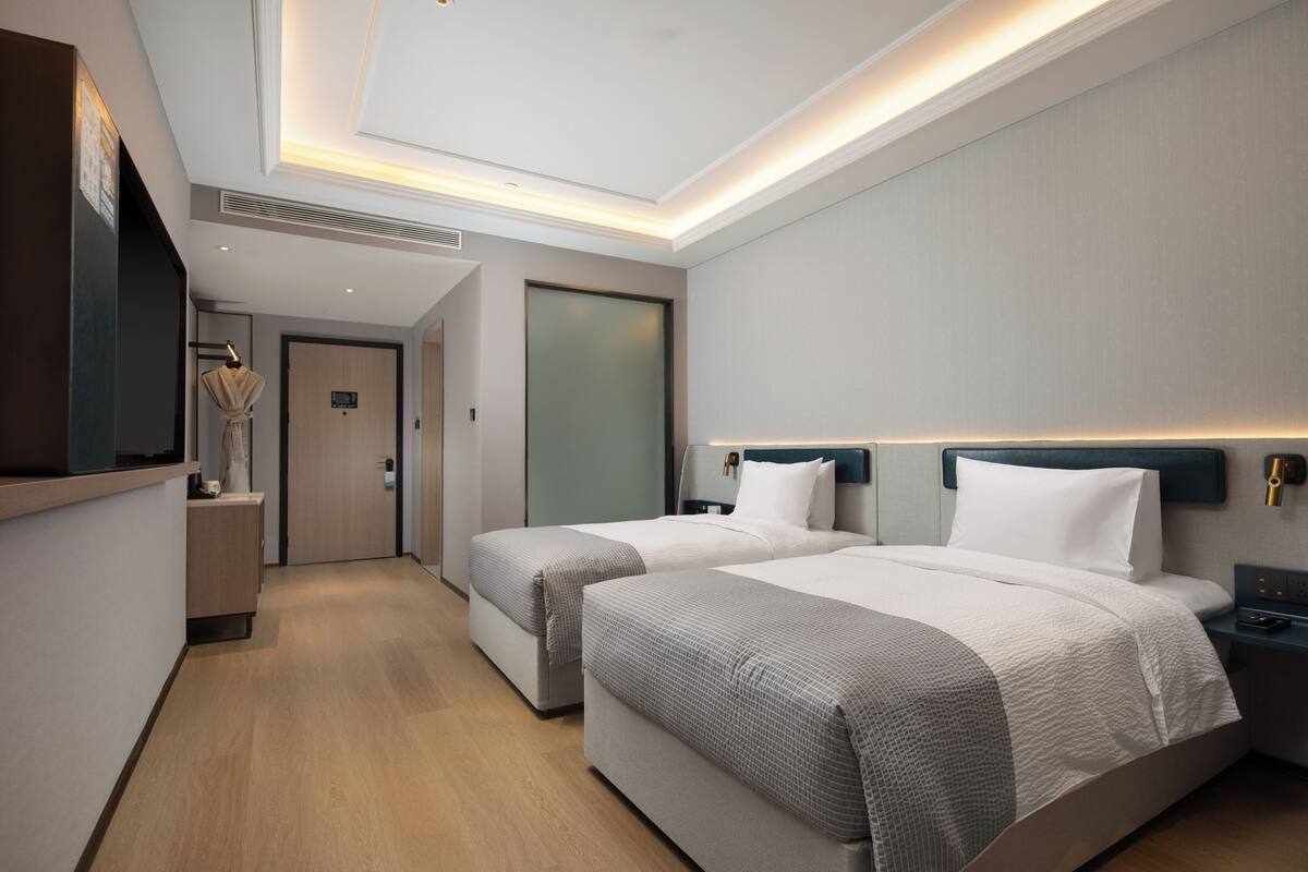 A modern hotel room with two beds, a small desk, and a mirror.