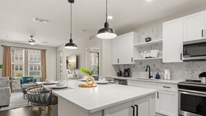 A modern kitchen with white cabinetry, a central island, pendant lighting, and a built-in oven.