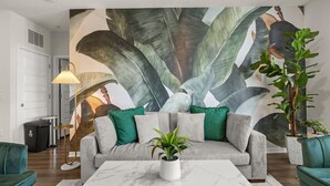 A living room with a sofa, a coffee table, a lamp, and a large wall mural.