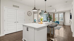 A modern kitchen with a white island, pendant lights, and a view to the living area.