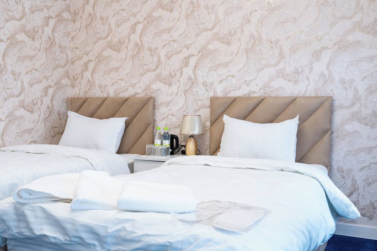 A hotel room with two beds, a nightstand, and a marble-patterned wall.
