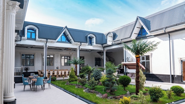 A courtyard with a seating area, a small garden, and a building with a blue roof and white columns. - GOLD STAR PALACE HOTEL (Samarkand)