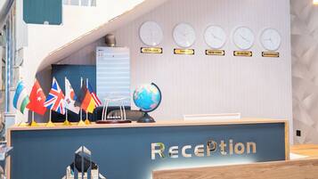 Mostrador de recepción en el hotel Gold Star, con banderas, relojes y un globo terráqueo.