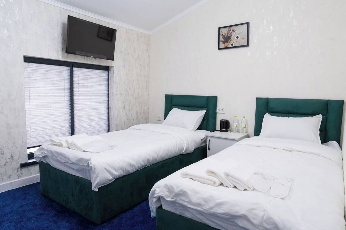 A hotel room with two beds, a TV mounted on the wall, and a window with blinds.