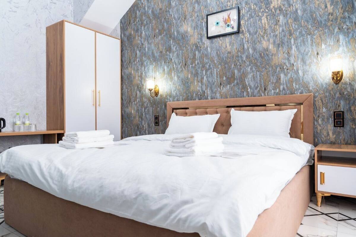 A neatly made bed with white linens and towels, a wooden wardrobe, and a wall with a textured pattern.
