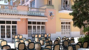 Un área de café al aire libre con varias mesas y sillas, un restaurante llamado 'Terrassa' y un cartel que indica 'Apartments'.
