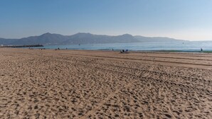 Una extensa playa de arena con cielo despejado y montañas a lo lejos.