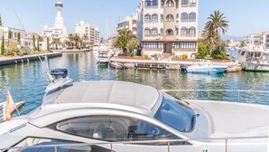 Un puerto deportivo con barcos amarrados, un edificio grande con varios balcones y un faro al fondo.