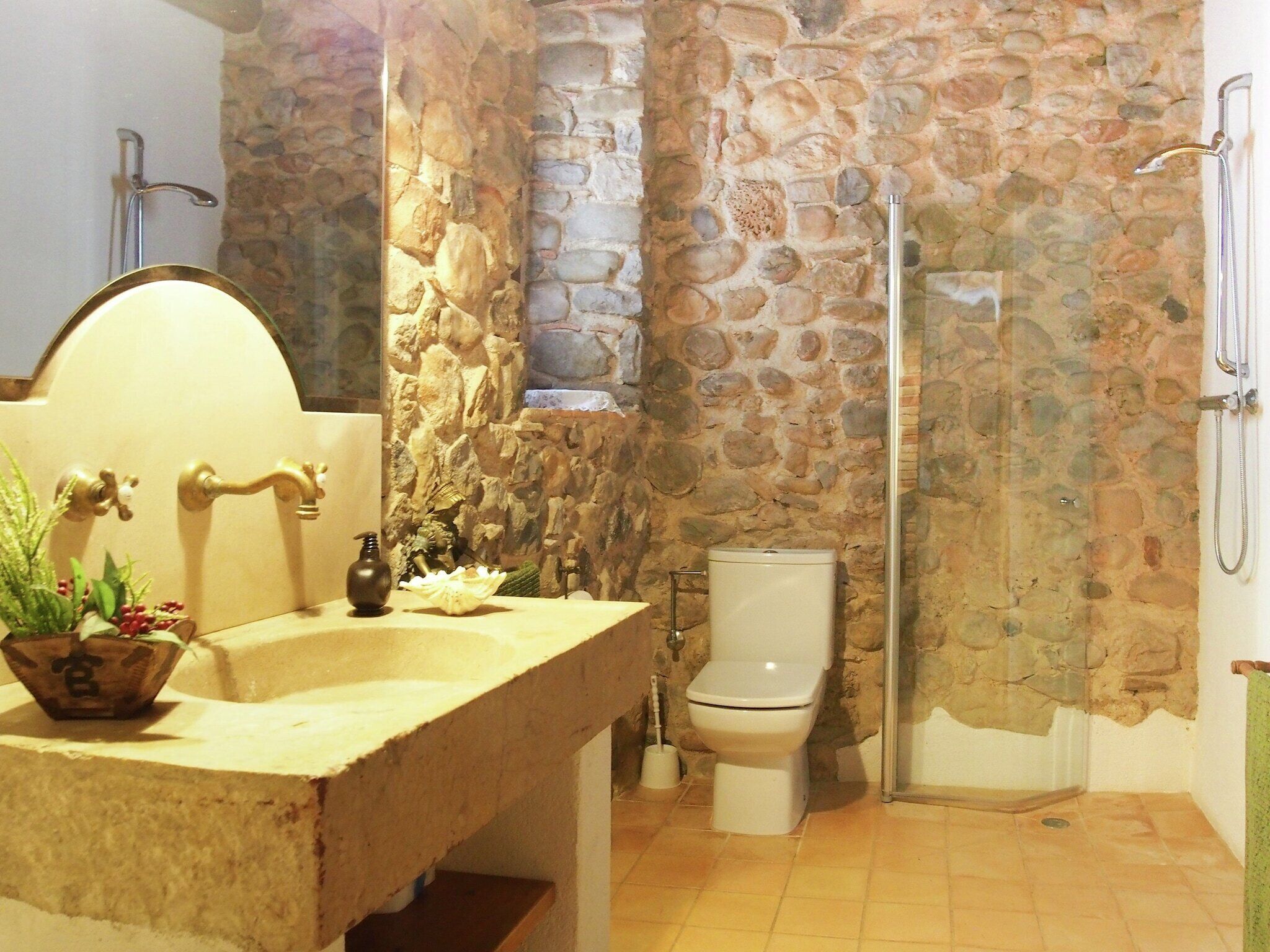 Un baño con pared de piedra, lavabo con espejo, inodoro y ducha.