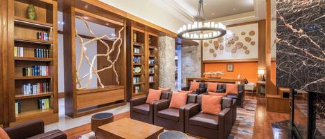 A spacious lobby with a central seating area, wooden bookshelves, a marble fireplace, and a modern chandelier.
