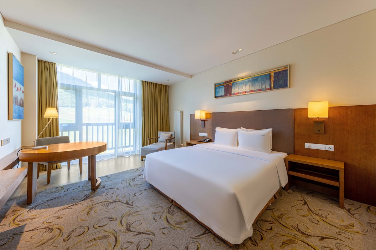 A hotel room with a large bed, a desk, two chairs, a lamp, and a painting on the wall.
