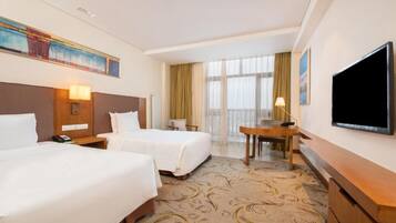 A hotel room with two beds, a desk, a TV, and a large window with curtains.