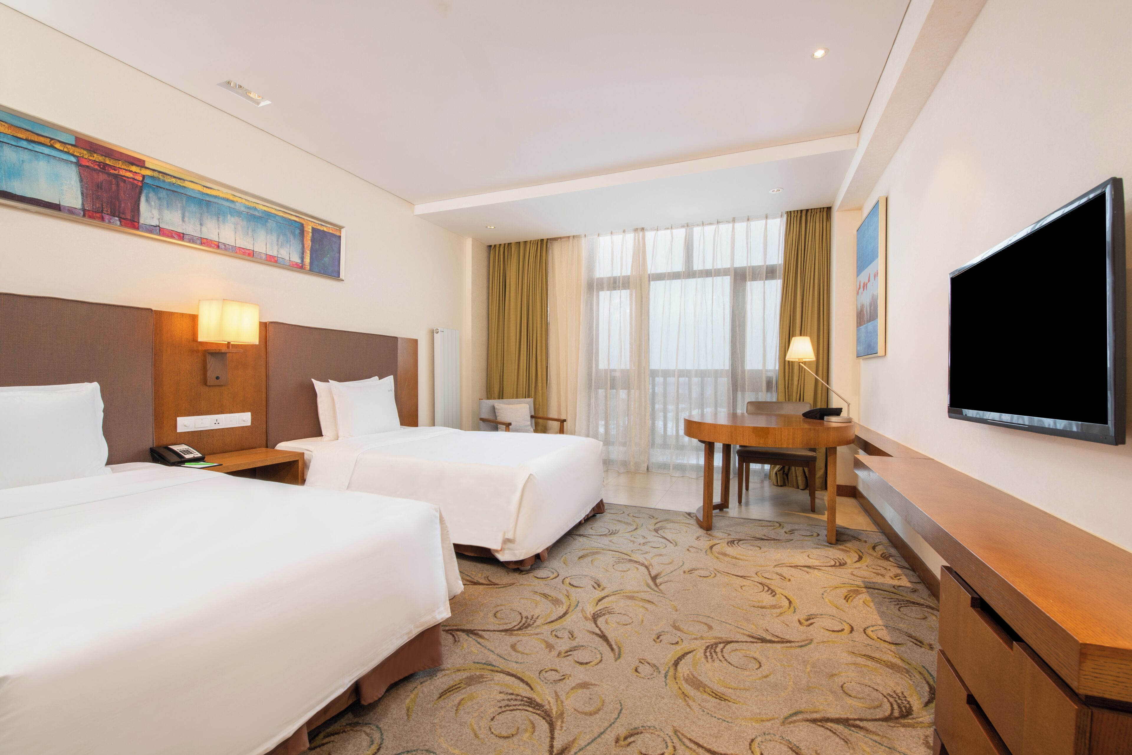 A hotel room with two beds, a desk, a television, and a painting on the wall.