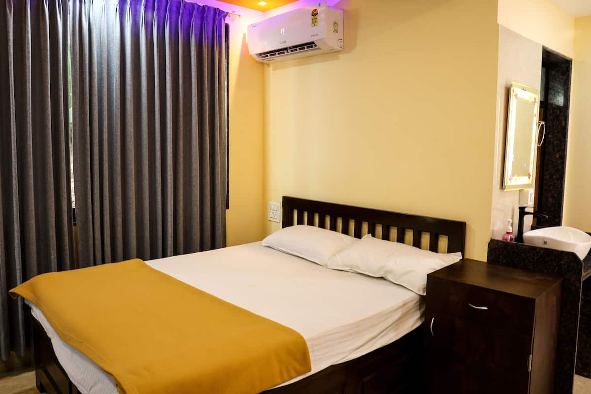 A hotel room with a bed, a nightstand, a mirror, and an air conditioning unit.
