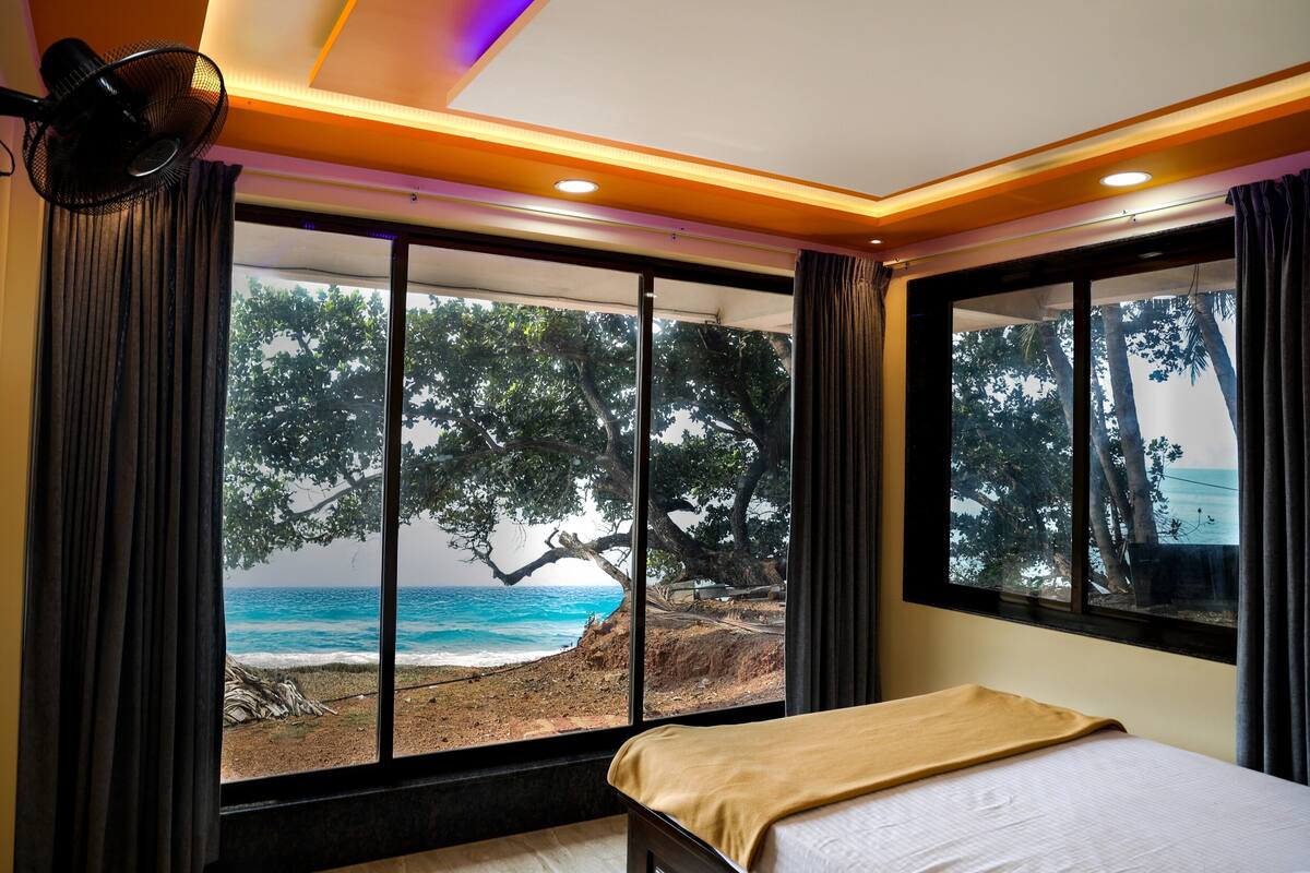 A bedroom with a large window offering a view of the beach and ocean.