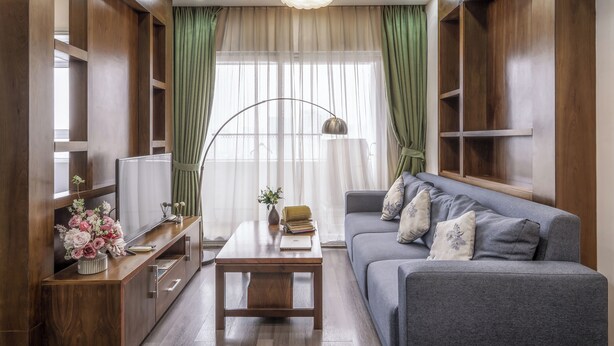 A modern living room with a grey sofa, wooden shelves, a TV, and a coffee table with a vase of flowers.