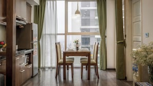 A dining area with a wooden table and chairs, a window with curtains, and a view of the city.