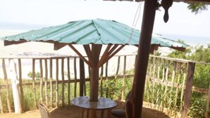 A covered outdoor seating area with a table and chairs, surrounded by a wooden fence and a view of greenery.