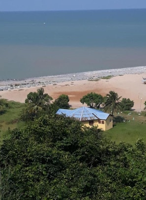A coastal view with a single-story building, a beach, and palm trees.