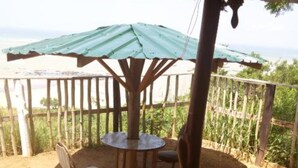 A covered outdoor seating area with a table and chairs, surrounded by a wooden fence and a view of greenery. - Special Place For Special People - room 5 (Abuesi)