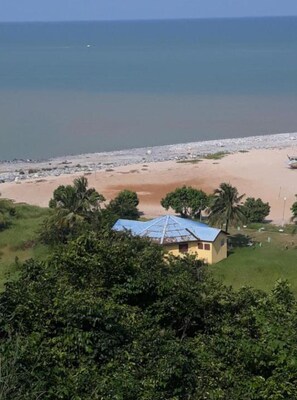 Une vue sur la côte, avec un bâtiment d’un seul étage, une plage et des palmiers.