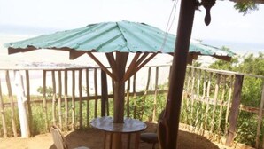 Un espace extérieur aménagé, abrité et doté d’une table et de chaises, entouré d’une clôture en bois et offrant une vue sur la verdure.