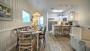 A dining area with a wooden table and chairs, a kitchen with white cabinets and stainless steel appliances, and a gray sofa.