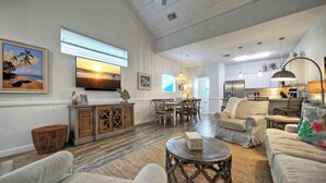 A spacious living room with a large TV, comfortable seating, a dining area, and a kitchen.