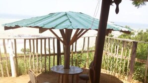 A covered outdoor seating area with a table and chairs, surrounded by a wooden fence and a view of greenery. - Special Place For Special People - room 8 (Abuesi)