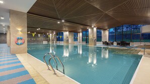 Une piscine intérieure à l’eau claire, dotée d’un sol carrelé et d’un plafond en bois.