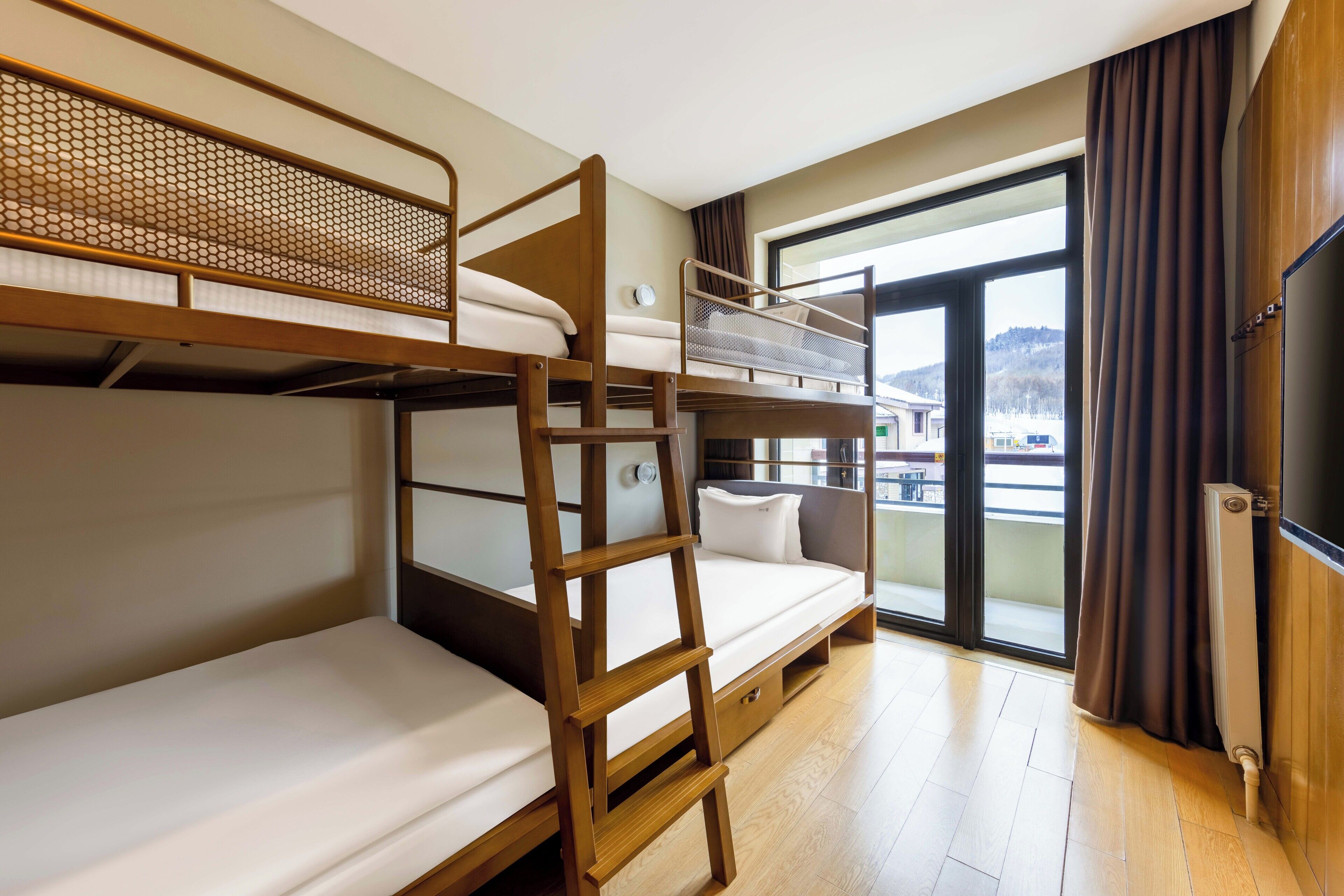 A bunk bed room with a ladder, a television, and a window with curtains.