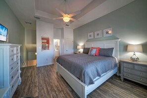 Une chambre à coucher comprenant un lit, une commode, une table de chevet et un ventilateur de plafond.