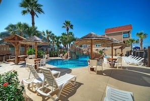 A pool area with lounge chairs, umbrellas, and a water feature.