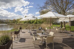 Relax on the patio with wicker chairs and tables, surrounded by trees and a serene water view.
