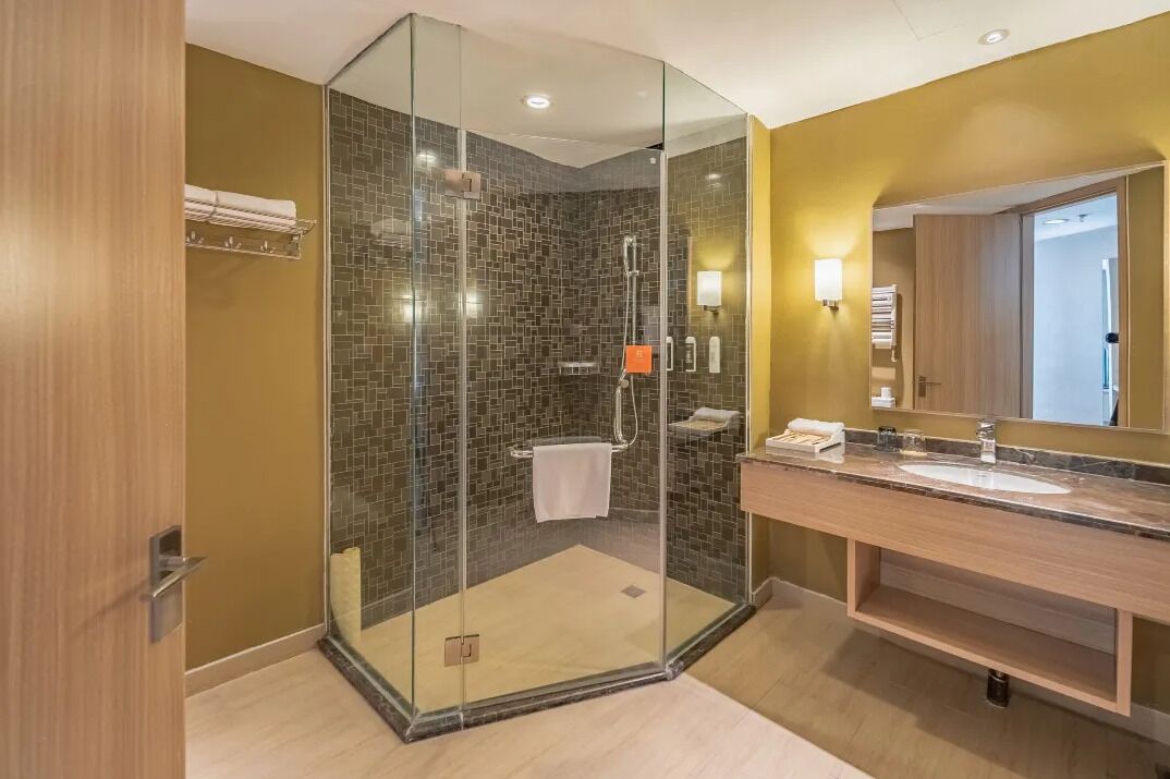 A modern bathroom with a glass-enclosed shower, a wooden vanity with a sink, and a large mirror.