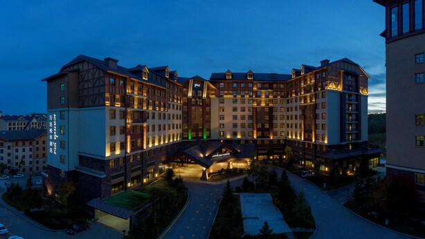 A multi-story hotel with a central courtyard, surrounded by parking and greenery. - Wanda Yue Changbaishan (Baishan)